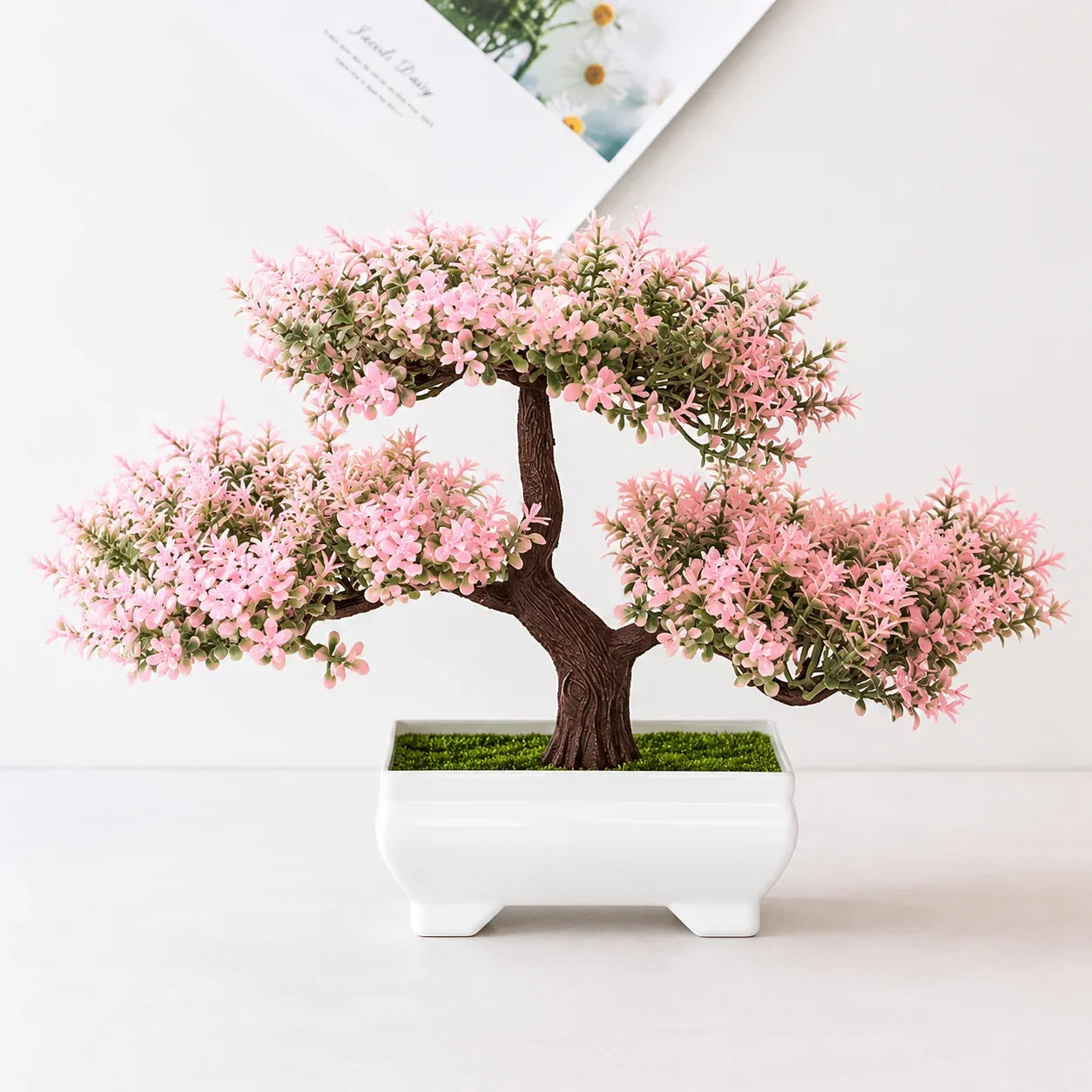 Pink flowering bonsai tree in white ceramic pot with green moss, for home or office decor