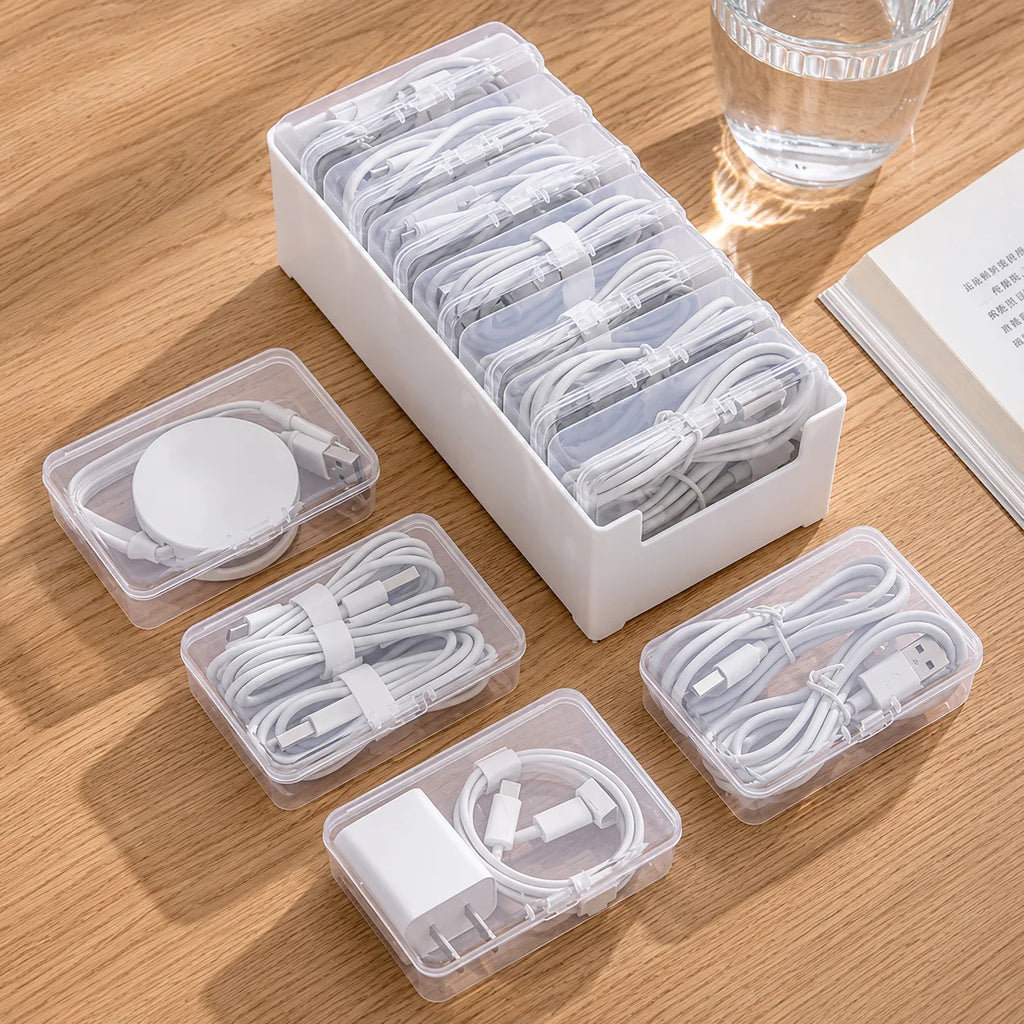 White plastic cable organizer with clear compartments holding neatly coiled charging cables and adapters on wood desk
