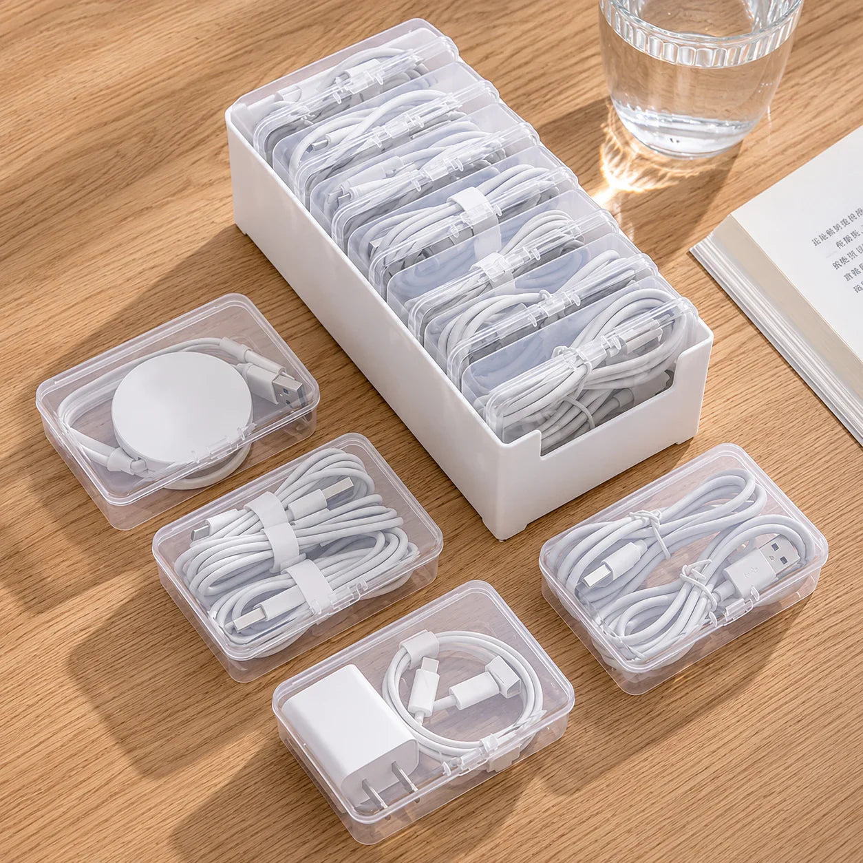 White plastic cable organizer with clear compartments holding neatly coiled charging cables and adapters on wood desk