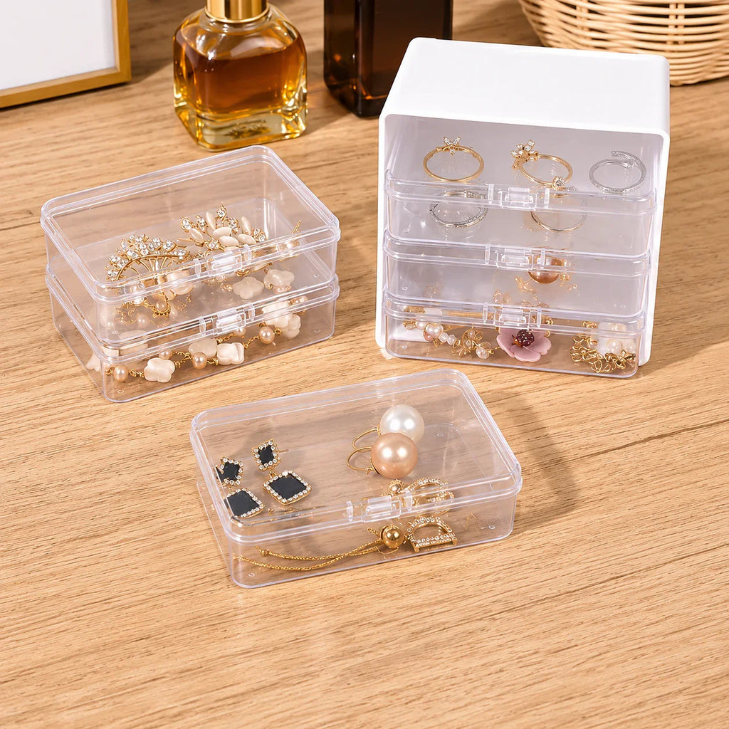 Clear plastic jewelry organizer boxes with white lids, storing rings, earrings, and necklaces on wood surface