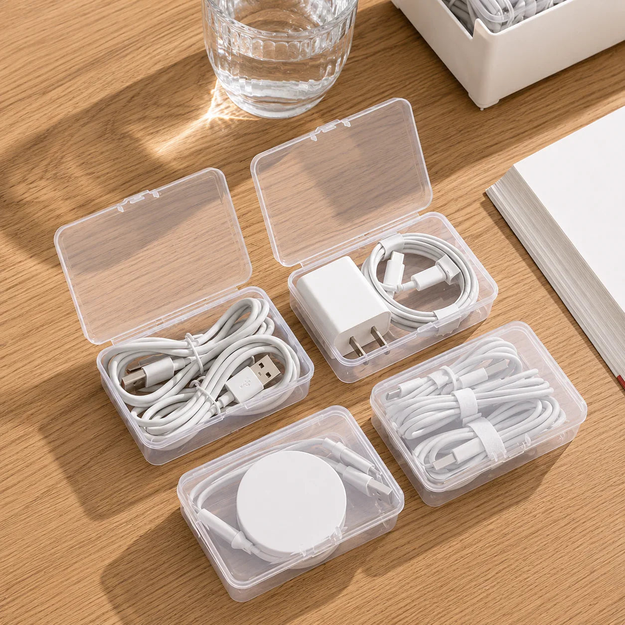 Clear plastic cable organizers storing white USB cords, charger, and wireless pad on wood desk