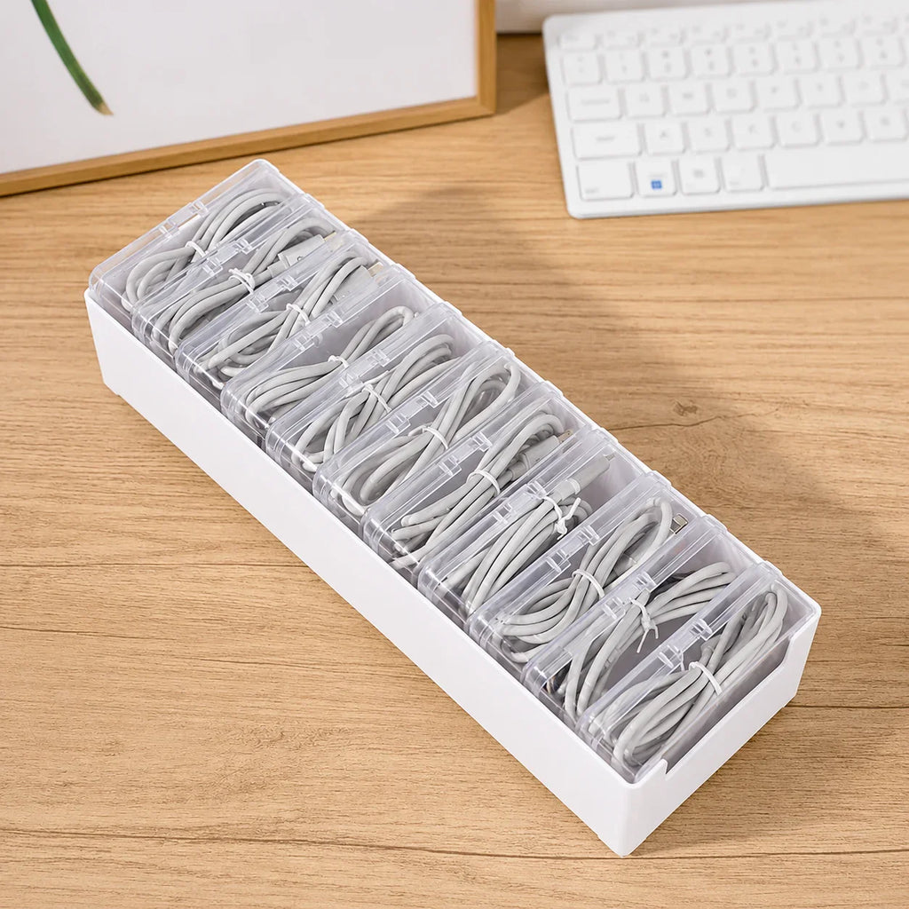 White plastic cable organizer with clear compartments holding neatly coiled gray charging cords on wooden desk