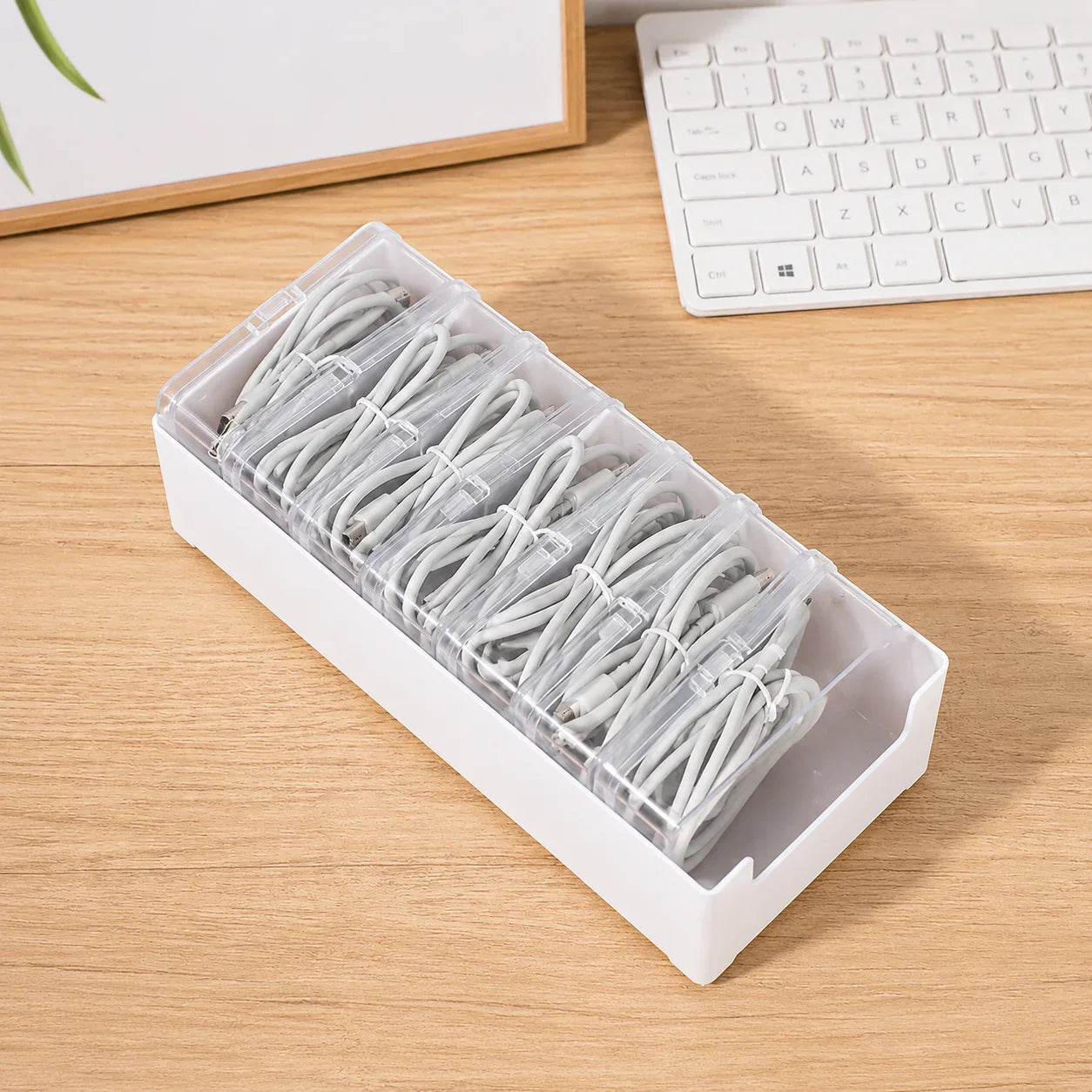 White plastic cable organizer with clear compartments holding neatly coiled white charging cords on wooden desk