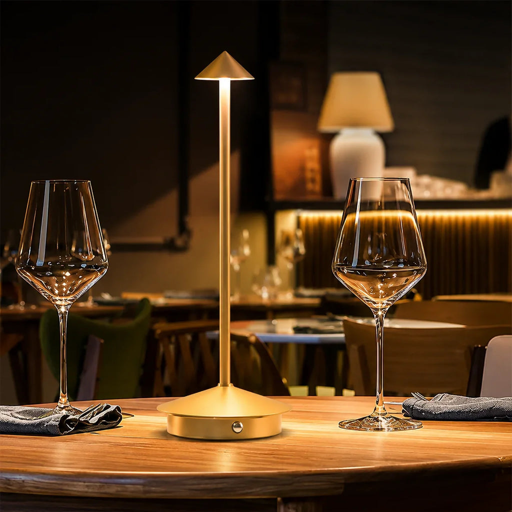 Golden modern table lamp with cone shade, illuminating dining table with wine glasses