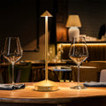 Golden modern table lamp with cone shade, illuminating dining table with wine glasses