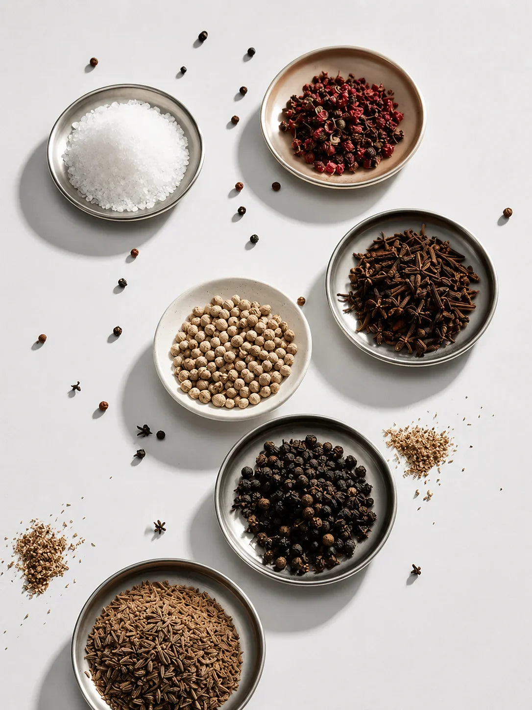 Assorted spices in ceramic bowls including salt, peppercorns, and cloves for kitchen seasoning