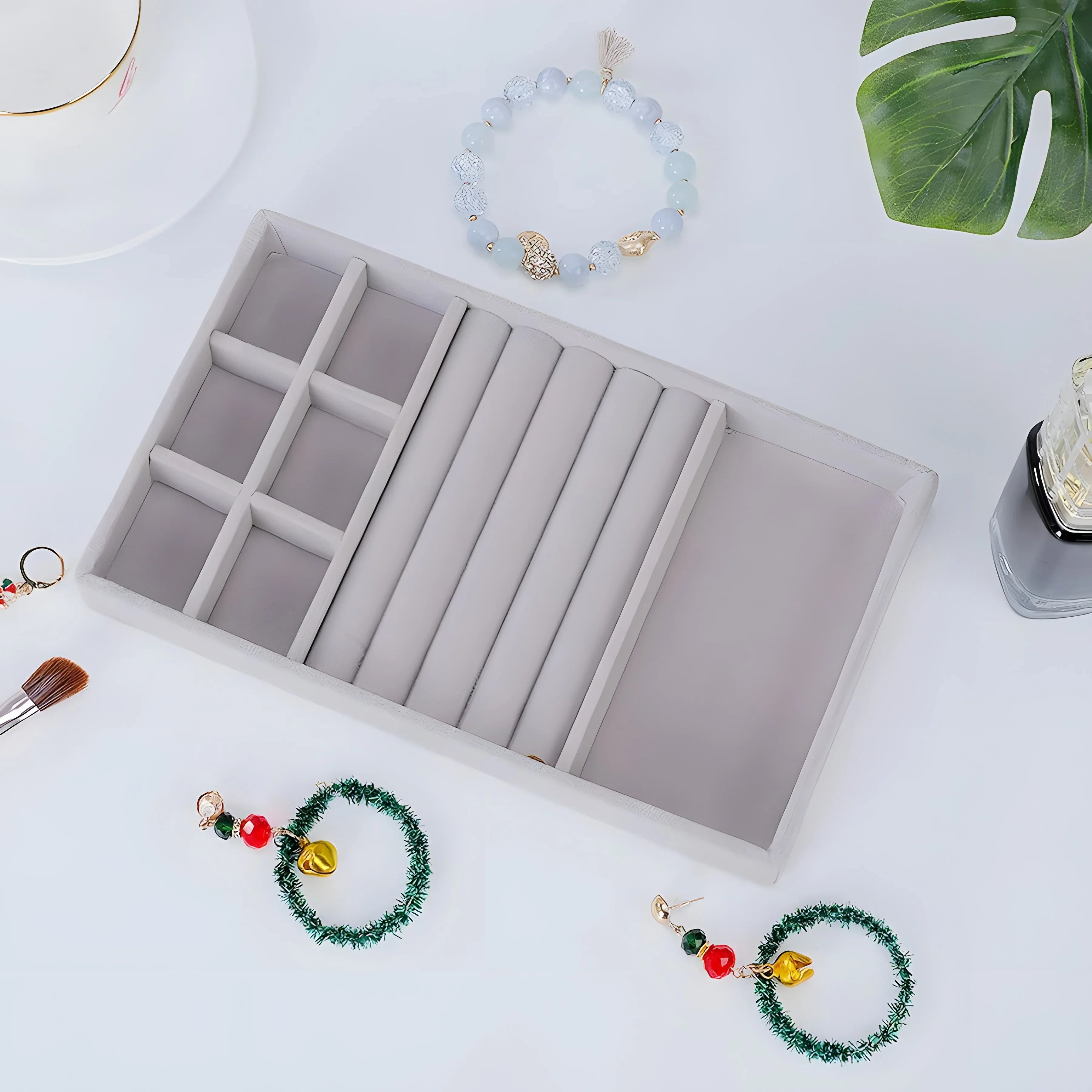 Gray velvet jewelry tray with compartments, holding festive green wreath earrings and a beaded bracelet