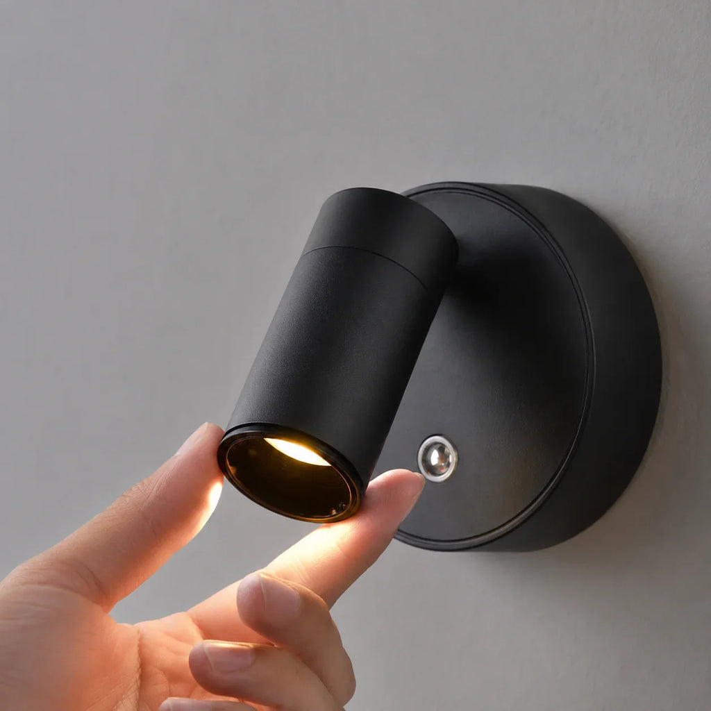 Black matte wall sconce with adjustable cylindrical head, emitting warm light for modern home lighting