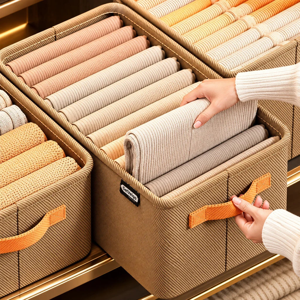 Hand organizing folded beige clothing in a GetVelqo fabric closet storage bin with orange handles.