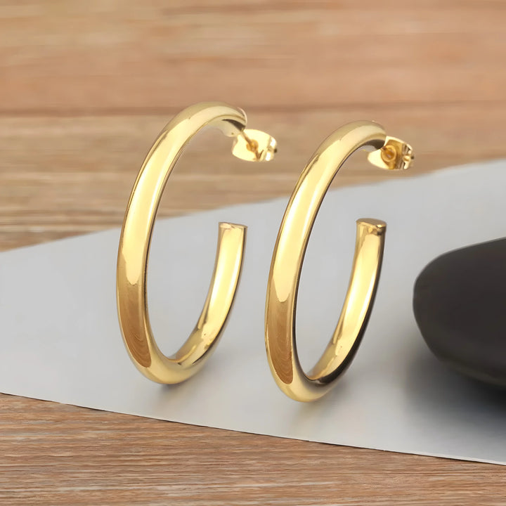 Minimal hoop earrings, gold-tone metal, sleek polished finish, modern minimalist style on wood surface.