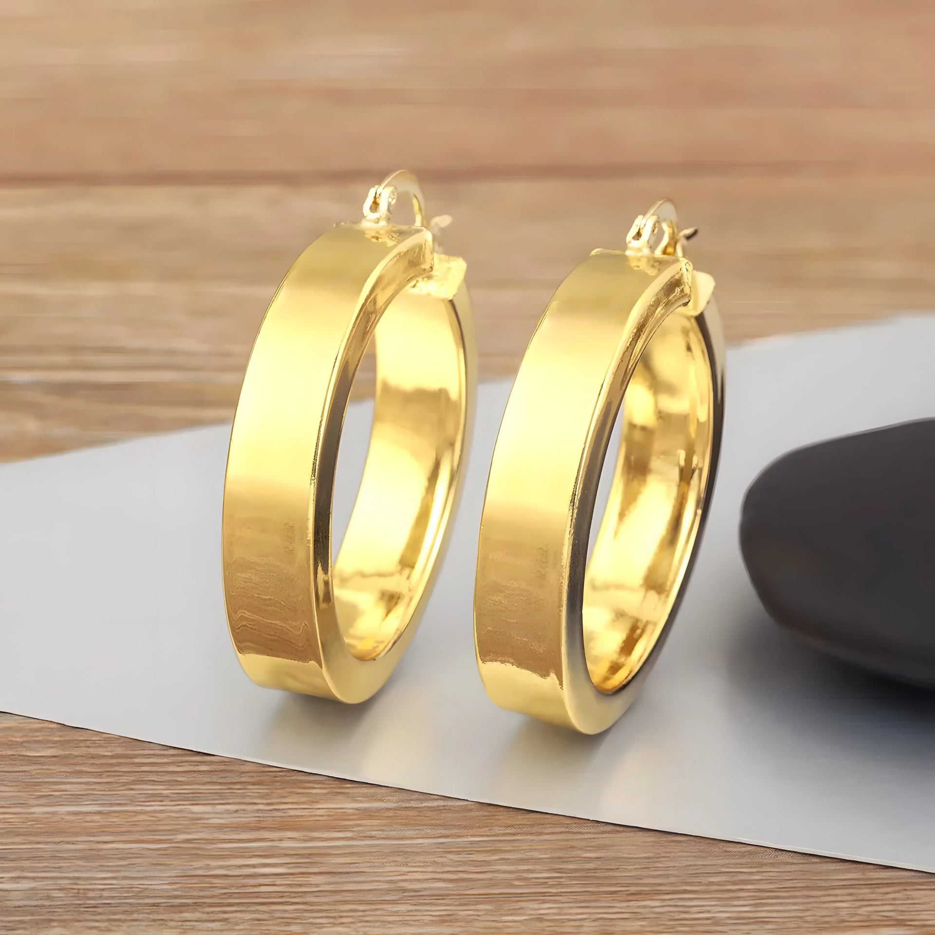 Minimal hoop earrings in gold tone, polished metal, modern and simple jewelry style on wood background.
