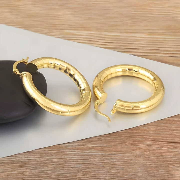 Minimal hoop earrings gold tone metal, chunky textured modern style on wooden surface
