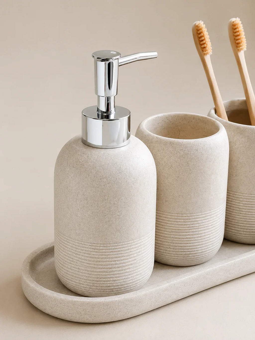 Beige ceramic soap dispenser with chrome pump, matching toothbrush holders, and tray for bathroom organization