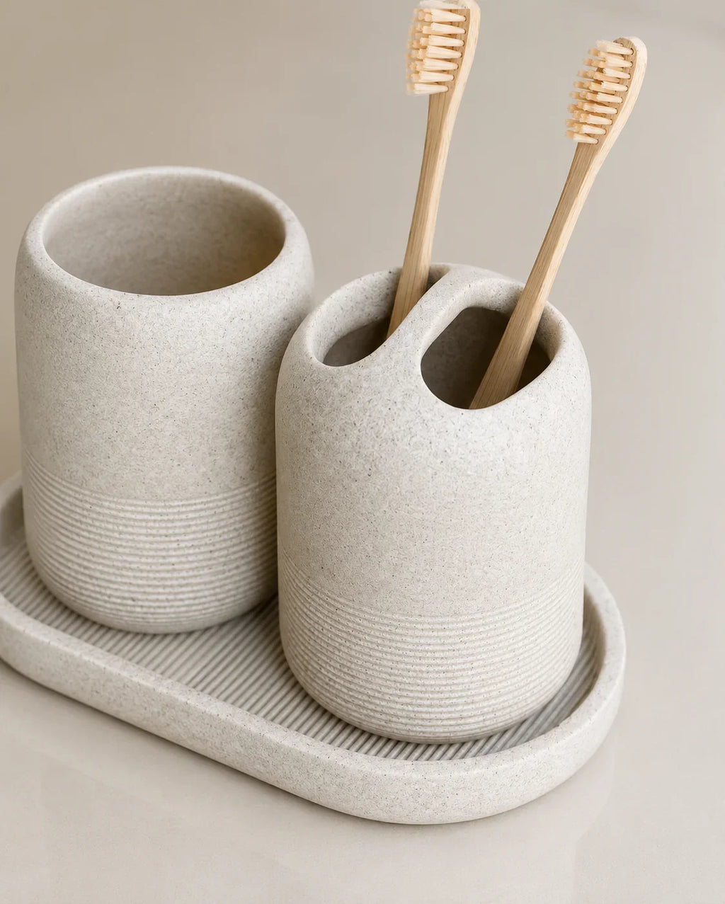 Beige speckled ceramic toothbrush holder with bamboo toothbrushes and matching cup on tray