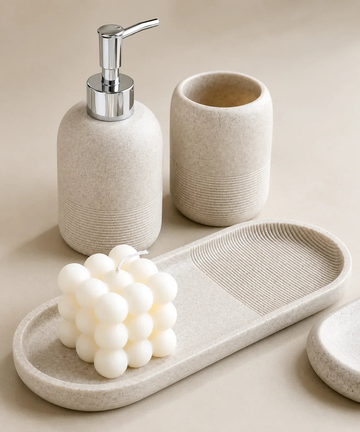 Beige textured soap dispenser, toothbrush holder, and tray with white candle for bathroom organization