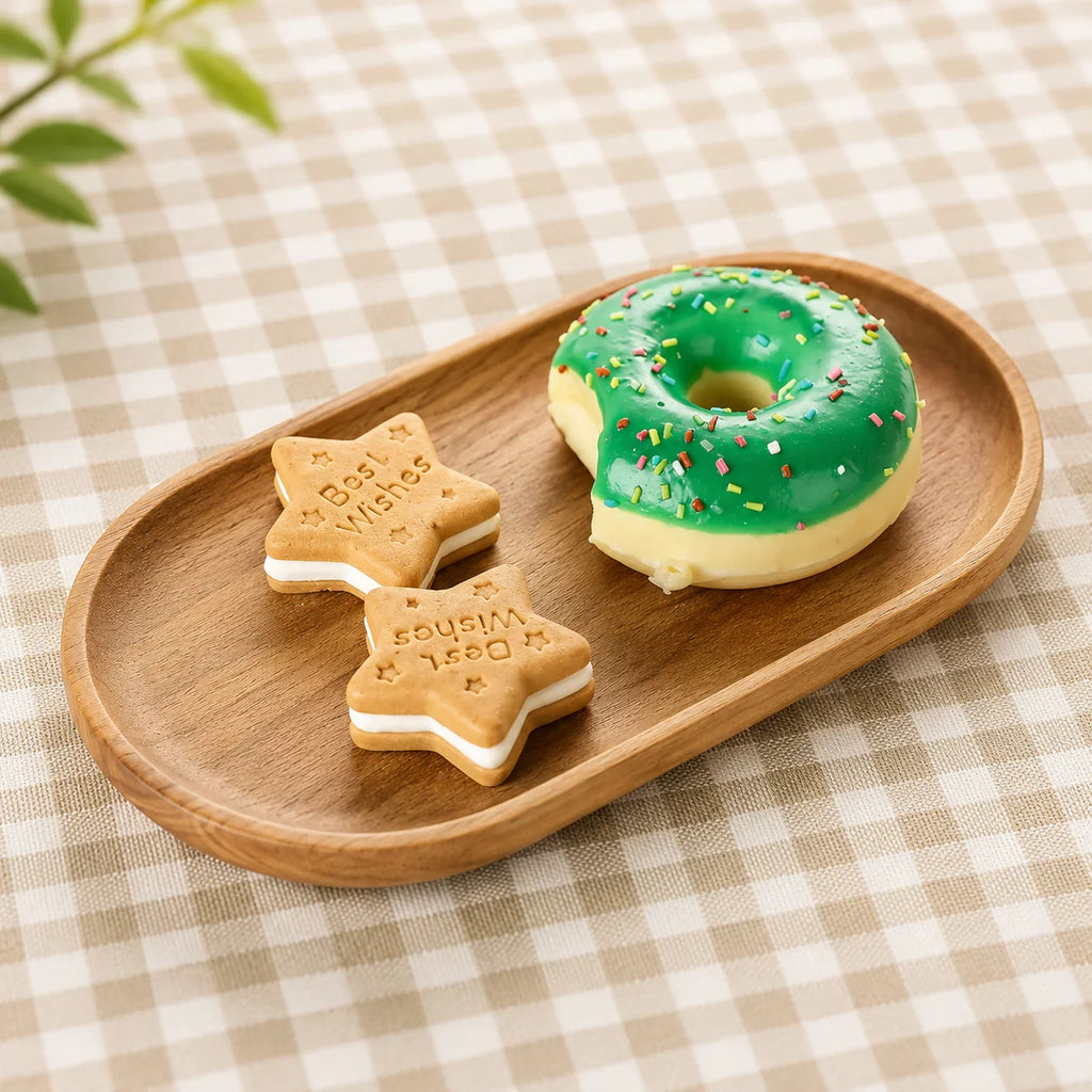 Wooden tray holding green frosted donut with sprinkles and star-shaped cookies on checkered tablecloth