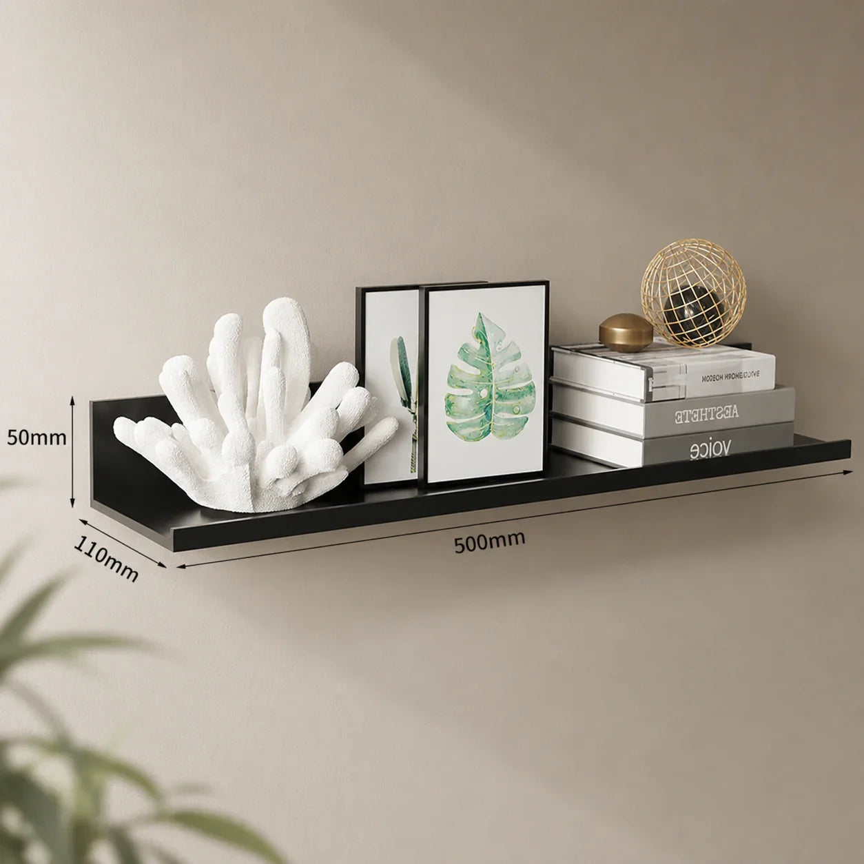 Black floating shelf with white coral decor, framed leaf art, and stacked books for modern home organization