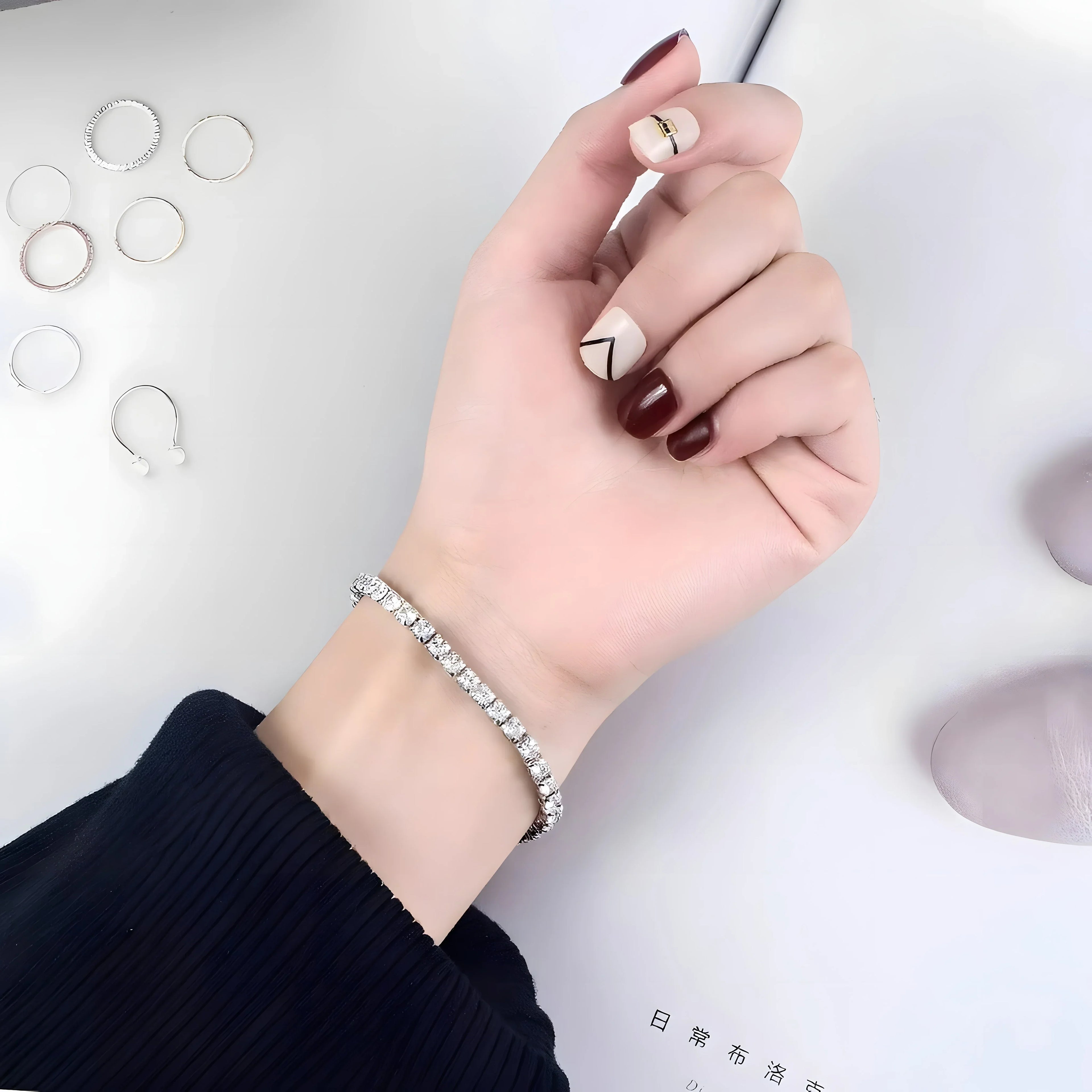 Silver tennis bracelet with clear crystals, minimalist style, worn on wrist with rings and manicure