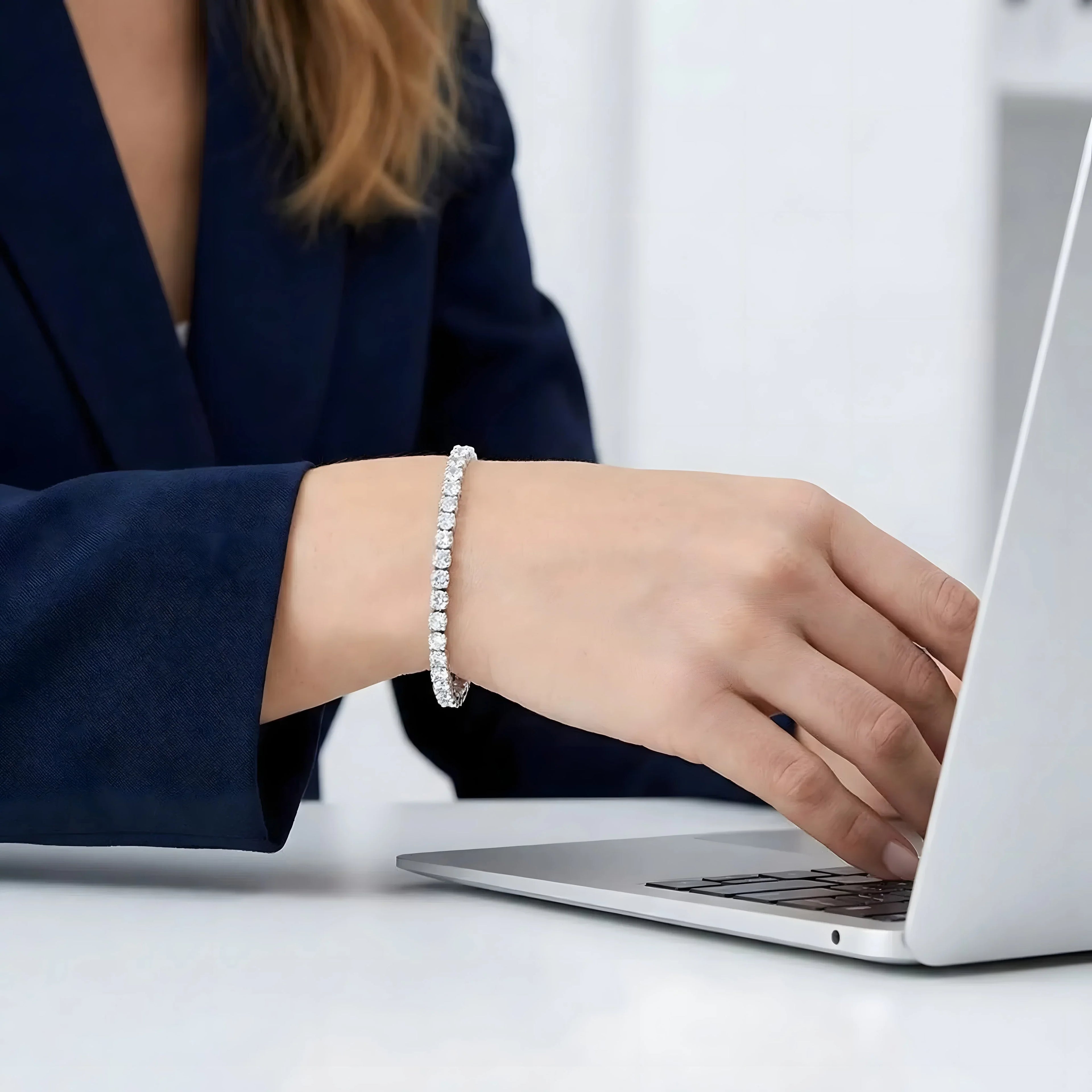 Elegant diamond tennis bracelet in silver, worn by woman typing on laptop, minimalist style