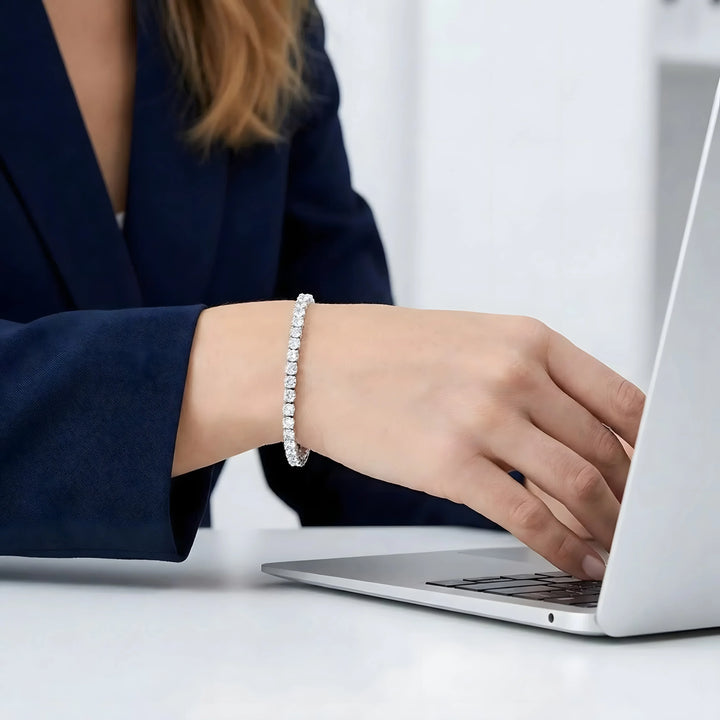 Elegant diamond tennis bracelet in silver, worn by woman typing on laptop, minimalist style