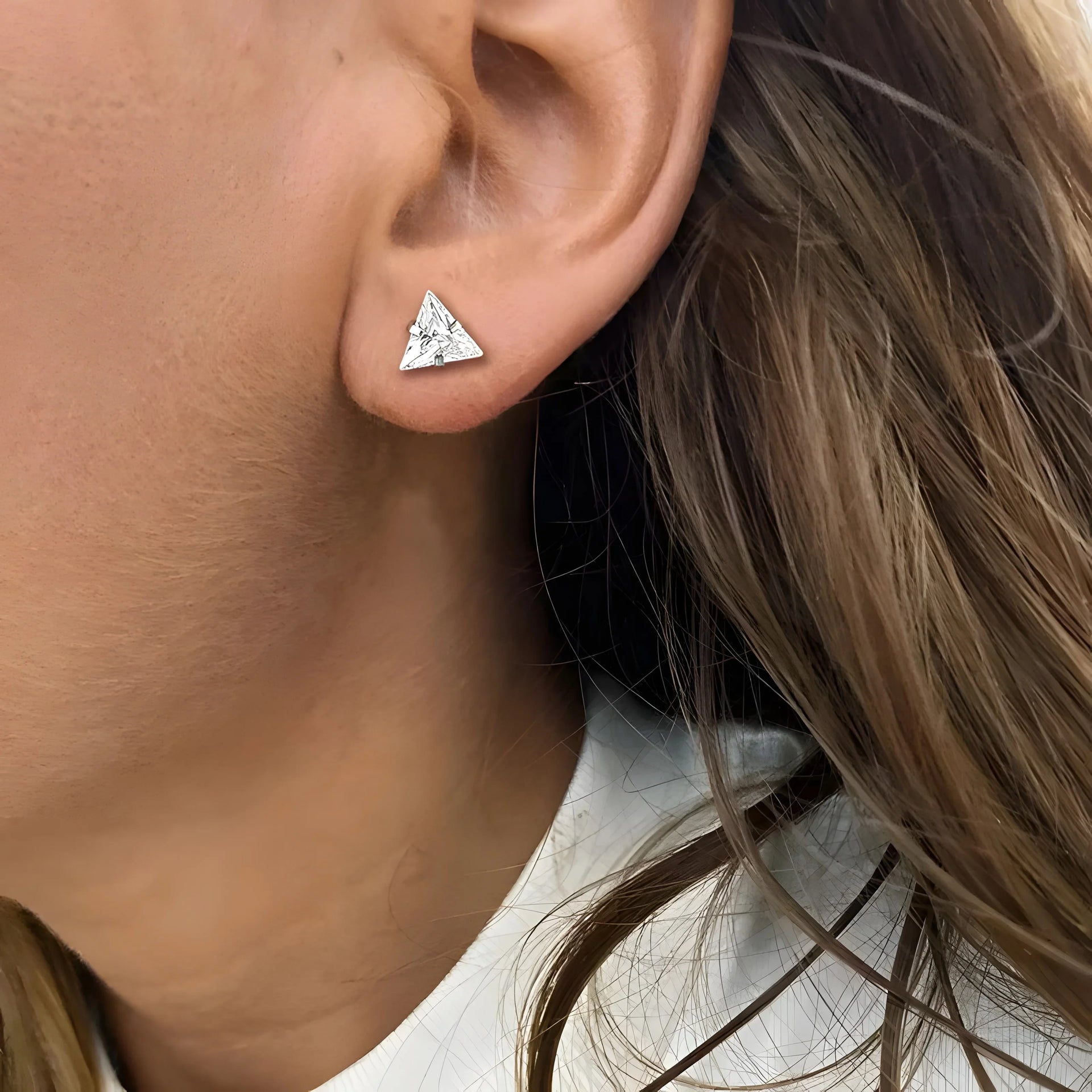 Silver triangle stud earring with geometric design, minimalist style, worn on earlobe