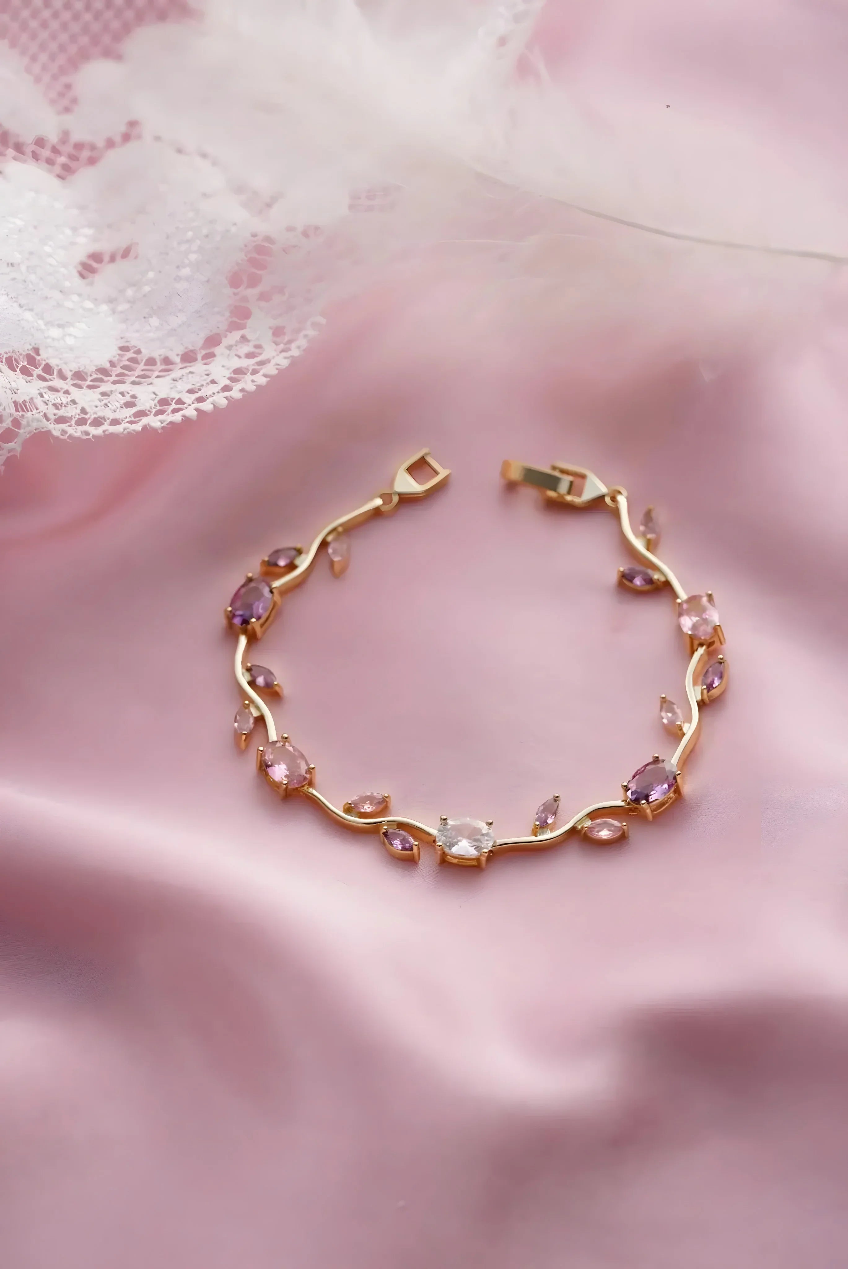 Gold bracelet with pink and clear gemstones, minimal vine design on soft pink fabric