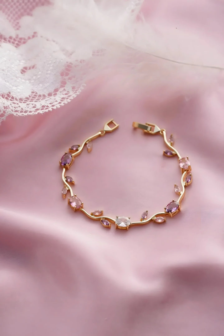 Gold bracelet with pink and clear gemstones, minimal vine design on soft pink fabric