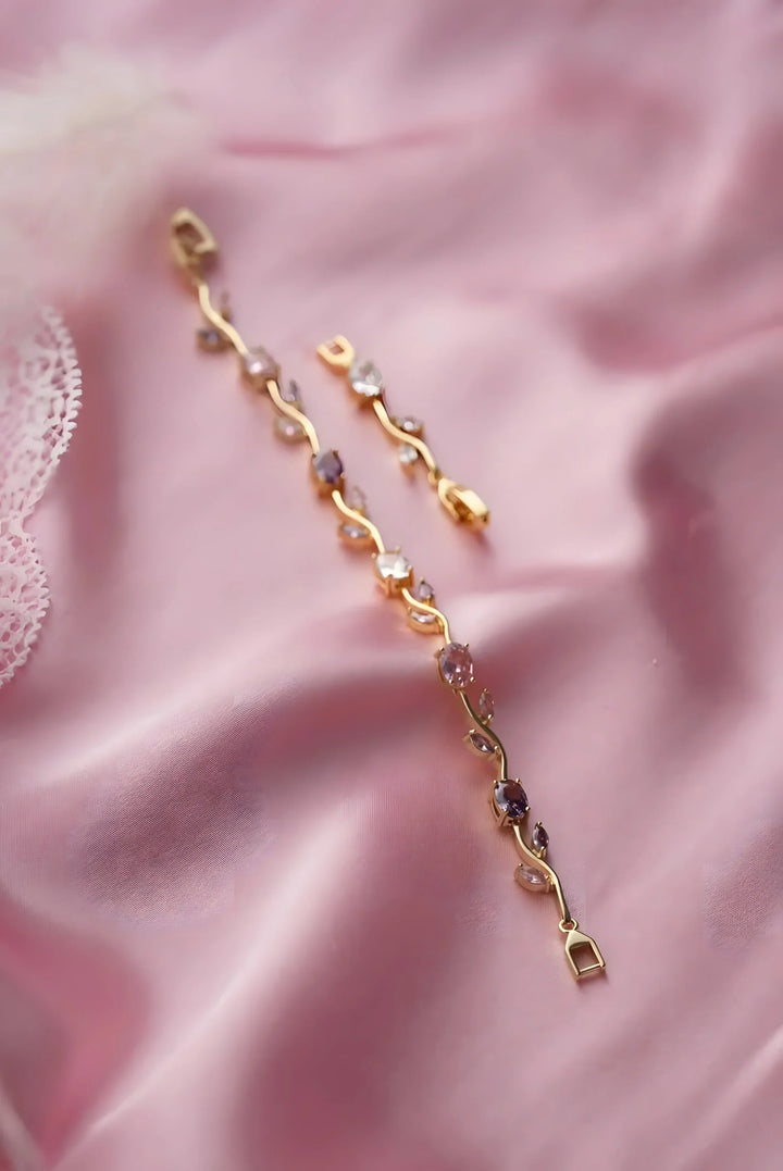 Gold vine-style bracelet with pink and clear gemstones on soft pink fabric, minimalist luxury jewelry