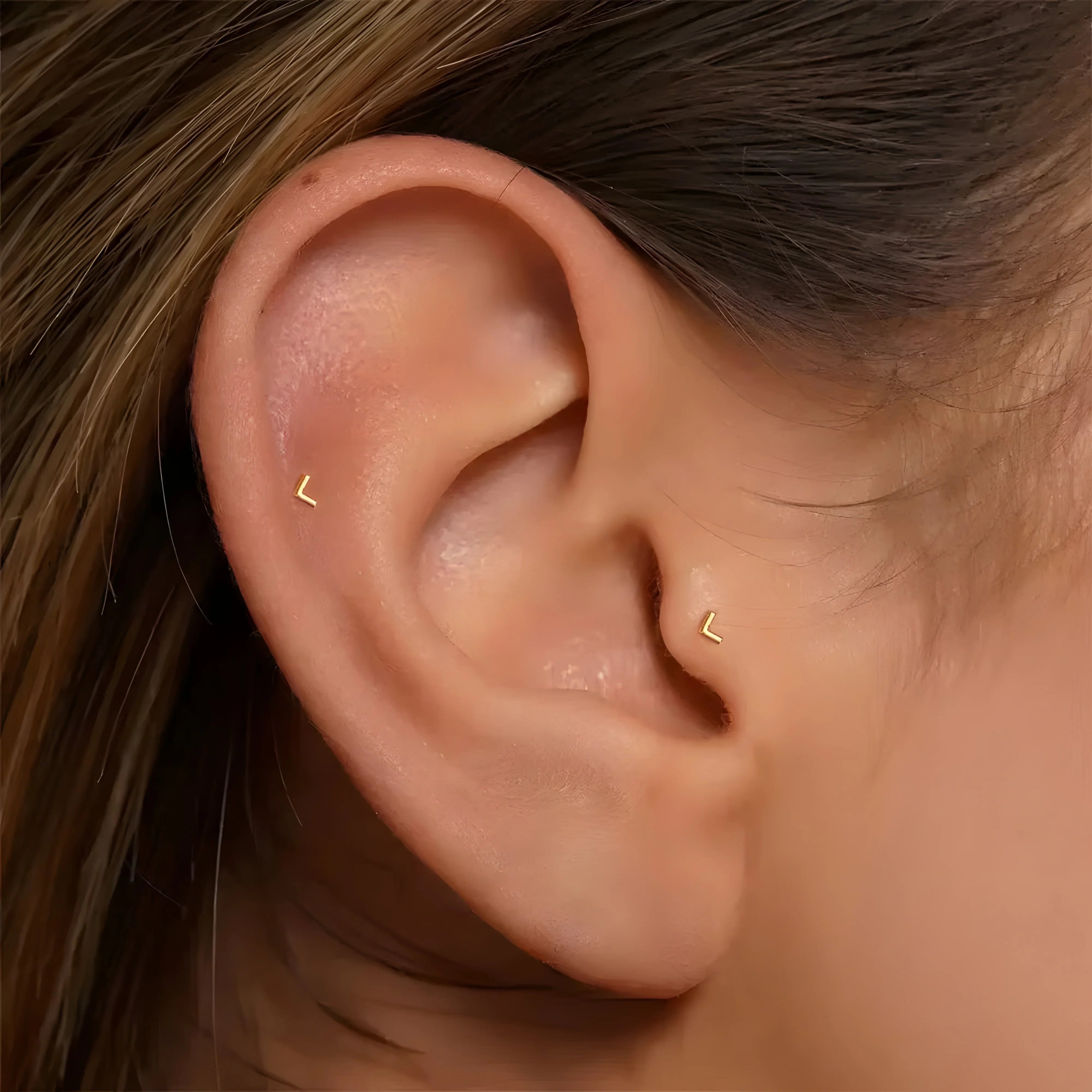 Minimalist gold zircon stud earrings in geometric V shape, worn on ear, modern style