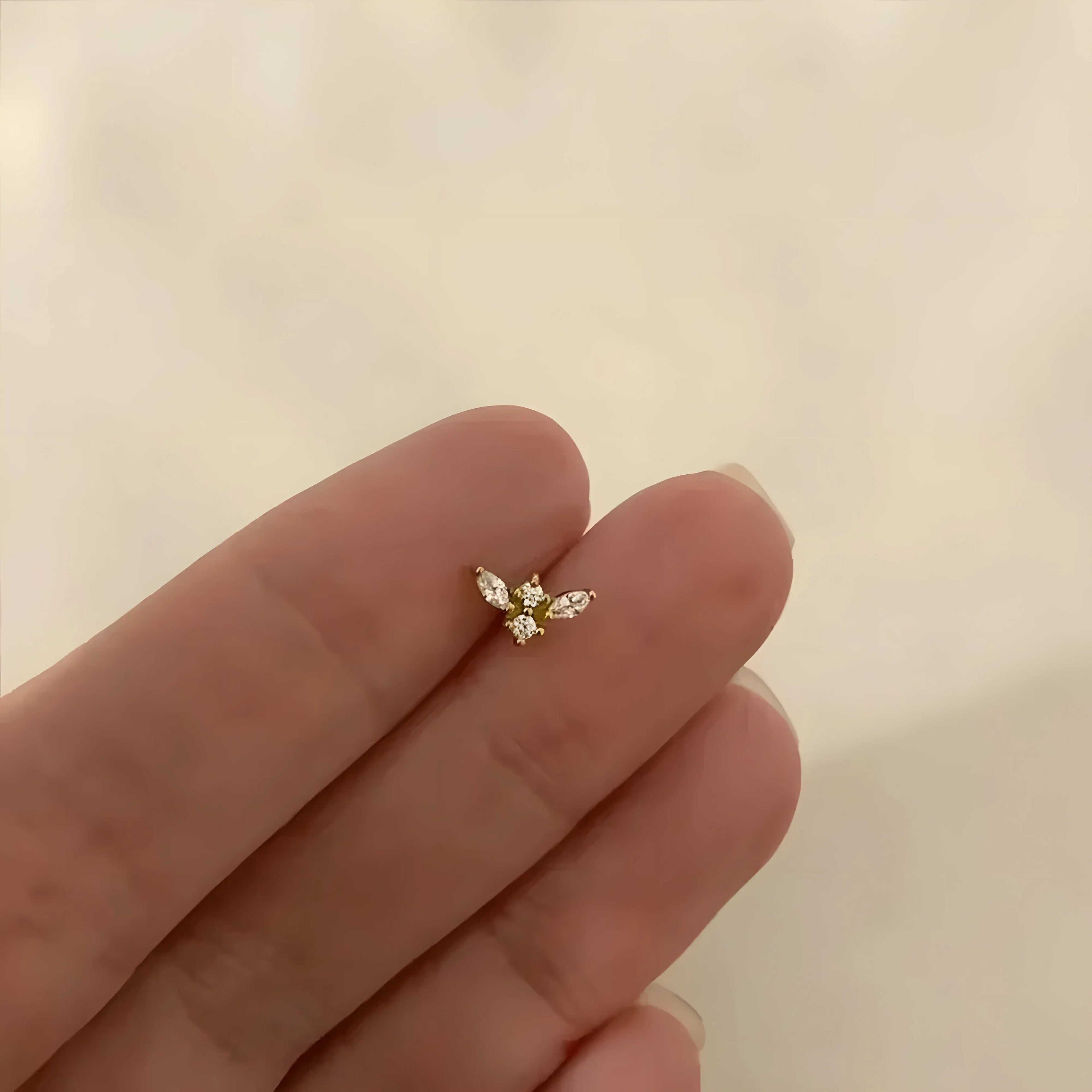 Zircon stud earring in gold, minimalist design with clear stones, shown on fingertip