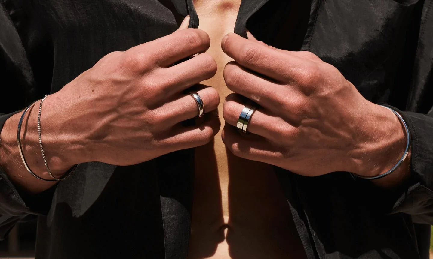 Silver men's rings and bracelets, minimalist style, worn on hands unbuttoning black shirt